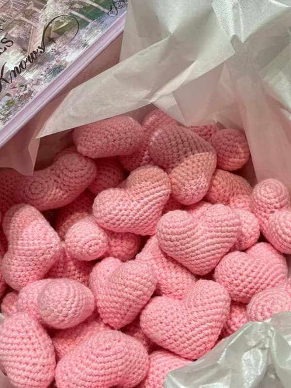 To lyserøde håndvævede hjerteformede bomuldsornamenter, dekoreret med ferskenhjerter, perfekte til Valentinsdag.