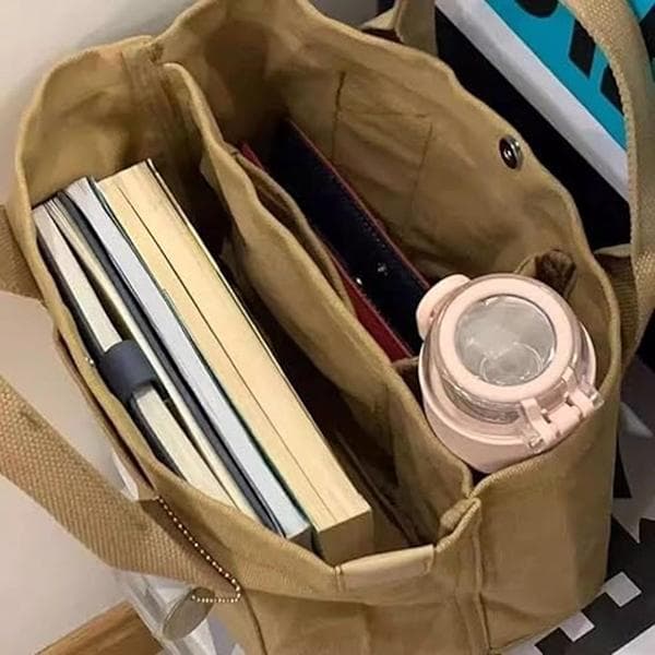 This khaki multi-compartment canvas tote bag features a gold charm and is spacious enough for books and everyday essentials.