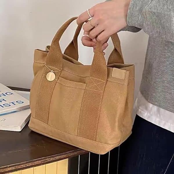 This khaki multi-compartment canvas tote bag features a gold charm and is spacious enough for books and everyday essentials.