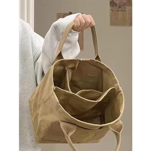 This khaki multi-compartment canvas tote bag features a gold charm and is spacious enough for books and everyday essentials.