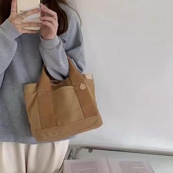 This khaki multi-compartment canvas tote bag features a gold charm and is spacious enough for books and everyday essentials.