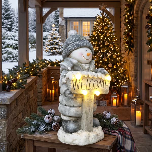 Upplyst snögubbe julstaty med välkomstskylt