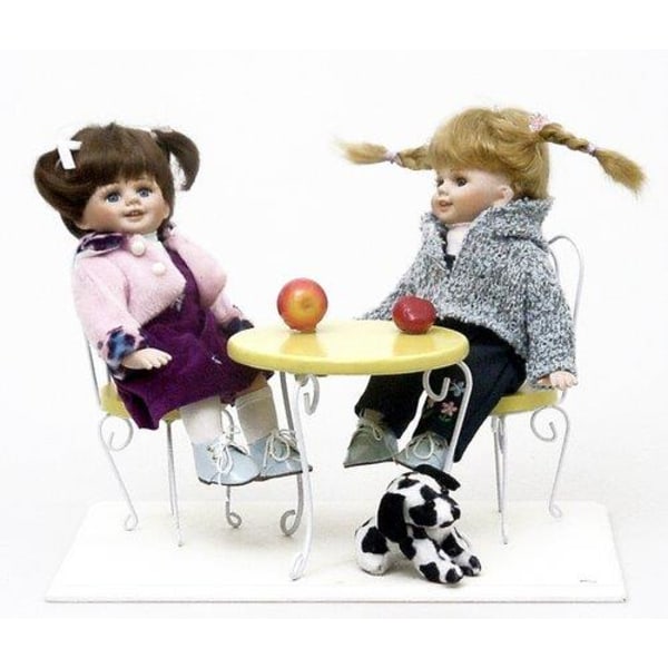Kaksi söpöä tyttönukkea istuu lankapuutarhapöydän ääressä