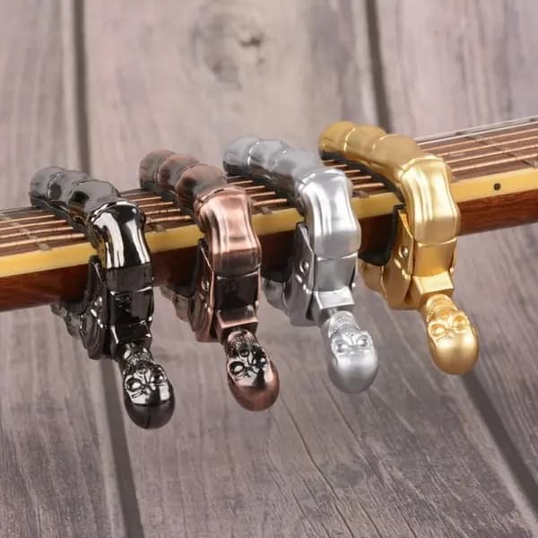 Gitar-capo i hodeskalledesign (egnet for akustiske og elektriske gitarer) samt ukulele-capo, gullfarget.